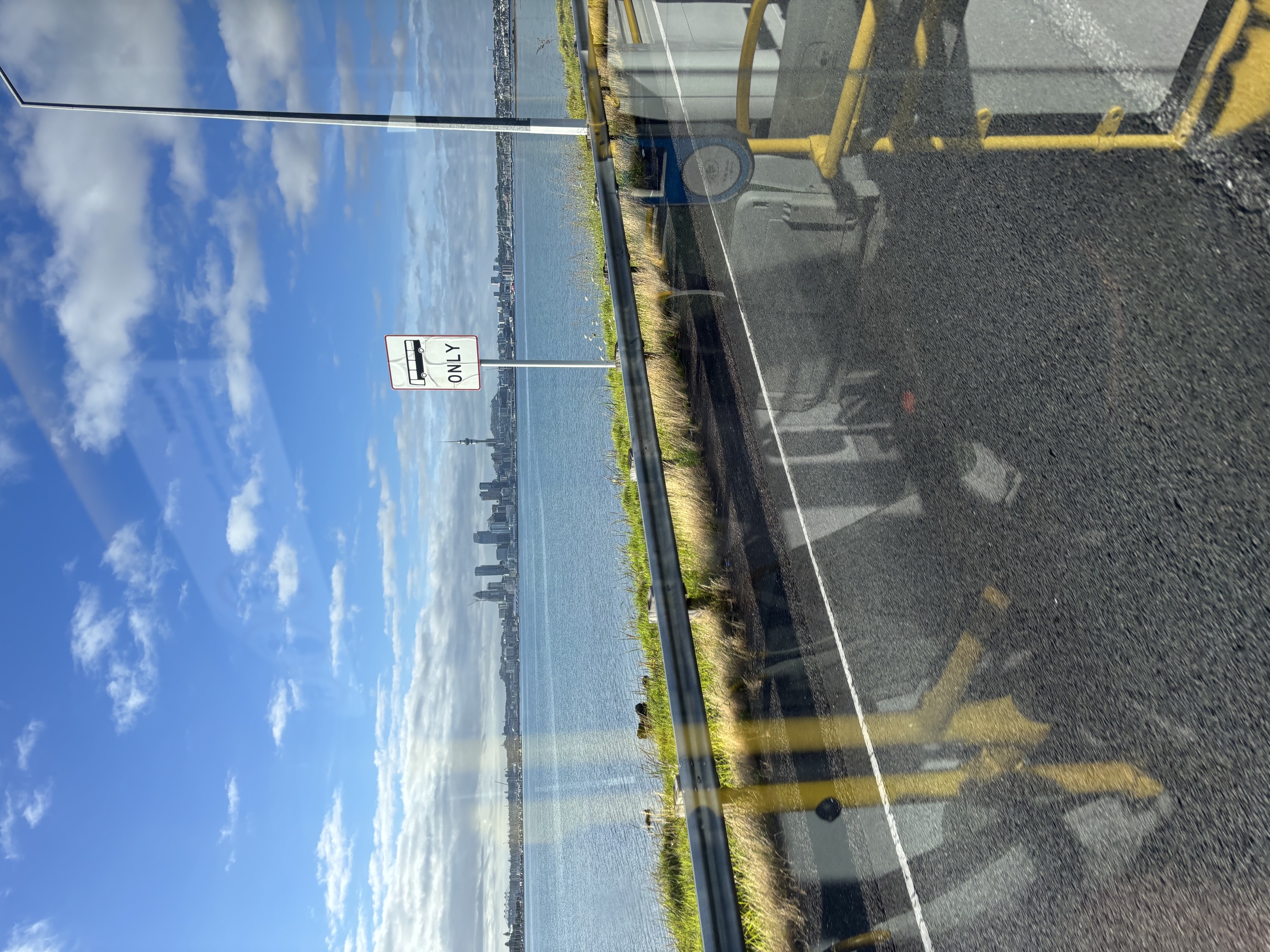 Auckland skyline and a bus-only sign seen through the reflections of a bus window.